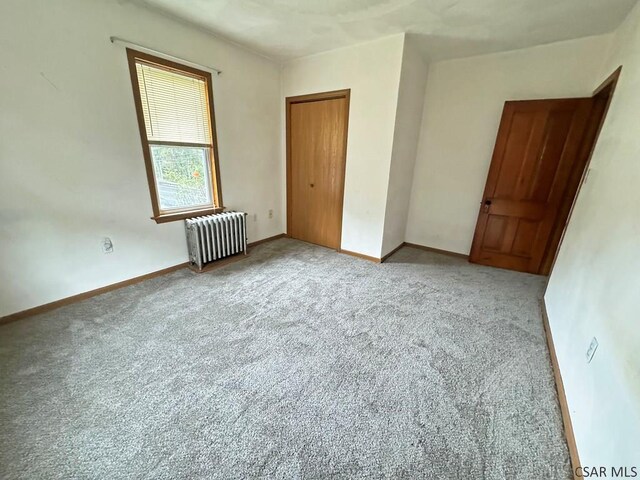 unfurnished bedroom with a closet, radiator, and carpet flooring