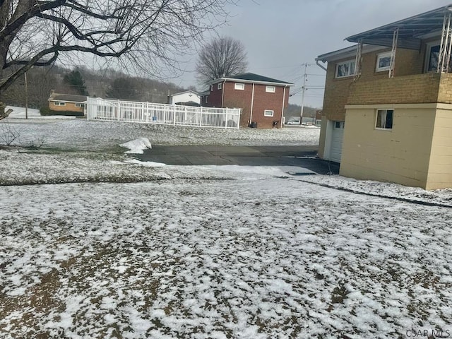 yard layered in snow with a garage, driveway, and fence