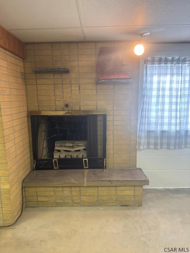 details with a drop ceiling, a fireplace with raised hearth, and unfinished concrete flooring