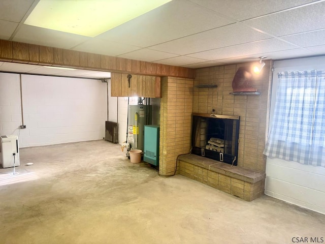 finished below grade area featuring a paneled ceiling, water heater, and concrete block wall