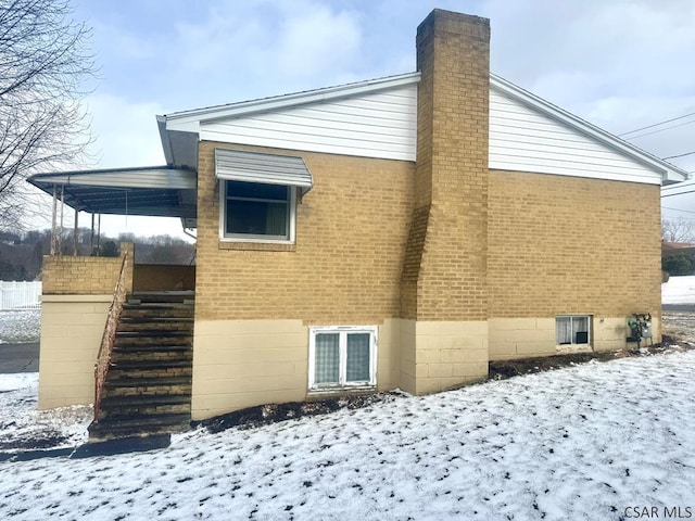 view of snowy exterior featuring a chimney and brick siding