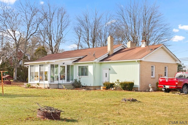 rear view of property with an outdoor fire pit, a yard, and a sunroom