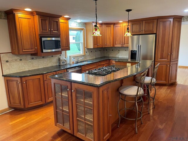 kitchen featuring decorative light fixtures, a center island, dark stone counters, stainless steel appliances, and light hardwood / wood-style floors