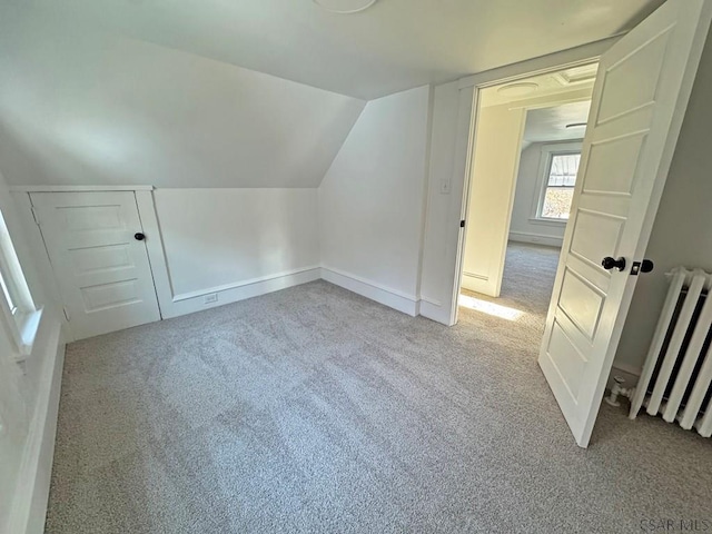 additional living space featuring light colored carpet, radiator heating unit, and vaulted ceiling