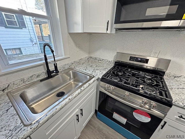 kitchen featuring appliances with stainless steel finishes, tasteful backsplash, sink, white cabinets, and light stone countertops