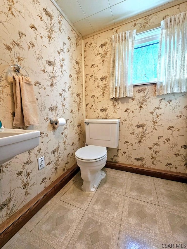 half bathroom featuring wallpapered walls, tile patterned floors, toilet, and baseboards