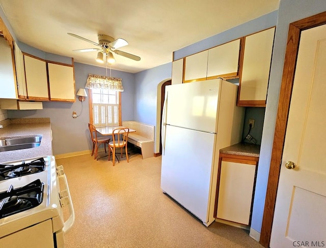 kitchen with baseboards, light countertops, white appliances, a ceiling fan, and a sink