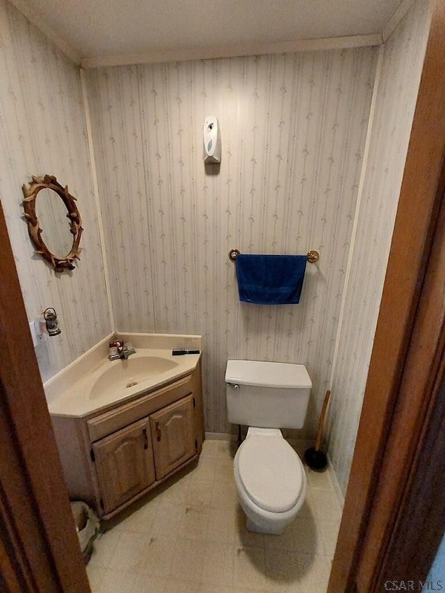 half bath featuring baseboards, vanity, toilet, and wallpapered walls