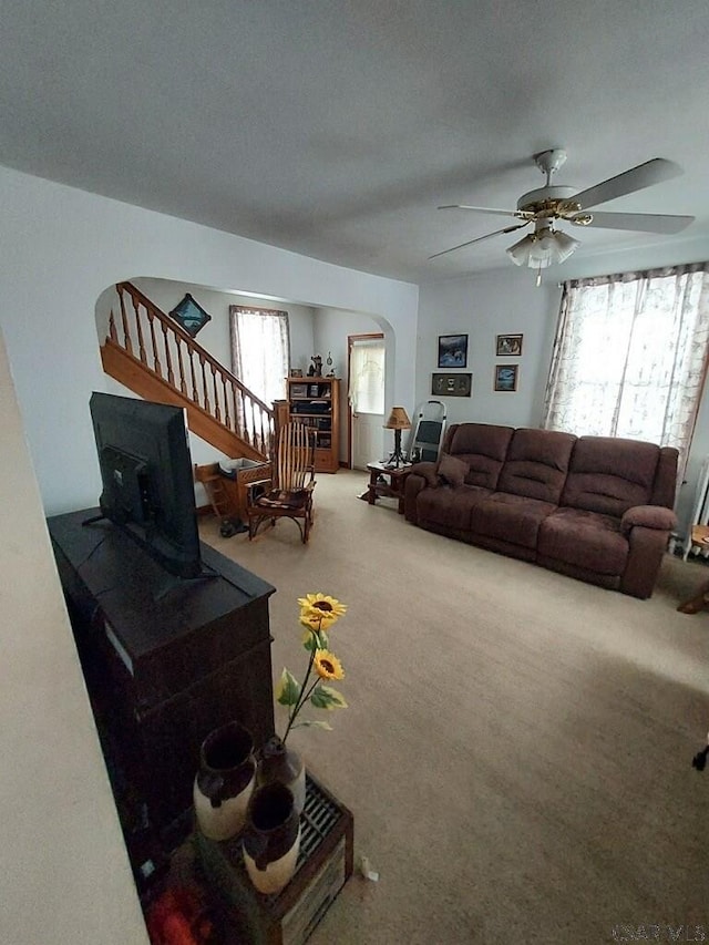 living area with carpet floors, stairway, ceiling fan, and arched walkways