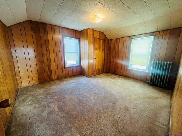 bonus room with wooden walls, radiator, vaulted ceiling, and light carpet