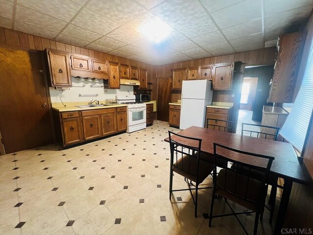 kitchen featuring white appliances, wooden walls, and sink