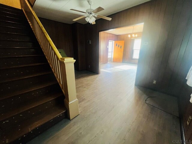 staircase featuring hardwood / wood-style flooring, wooden walls, and ceiling fan with notable chandelier