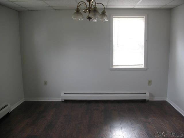 unfurnished room with an inviting chandelier, dark wood-type flooring, and baseboard heating