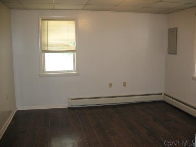 empty room with baseboard heating, dark hardwood / wood-style floors, electric panel, and a drop ceiling