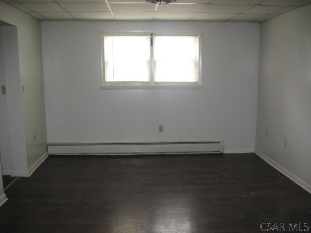 spare room featuring dark wood-type flooring, a paneled ceiling, and a baseboard heating unit