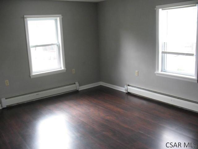 unfurnished room featuring dark hardwood / wood-style floors, a healthy amount of sunlight, and baseboard heating