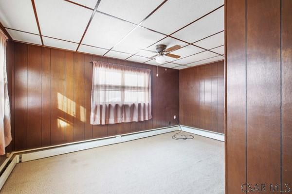 empty room with ceiling fan, wooden walls, a drop ceiling, and a baseboard heating unit