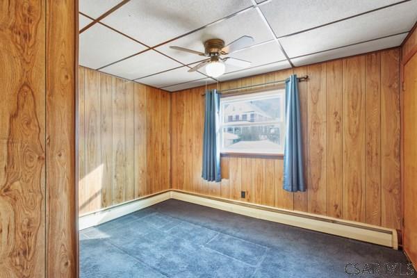 spare room with ceiling fan, a drop ceiling, and wooden walls