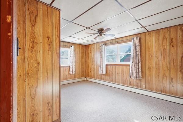 spare room with a drop ceiling, ceiling fan, and wood walls