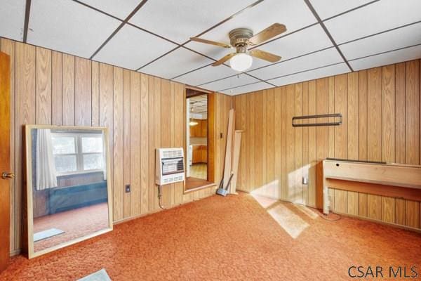 unfurnished living room with ceiling fan, wooden walls, carpet, and heating unit