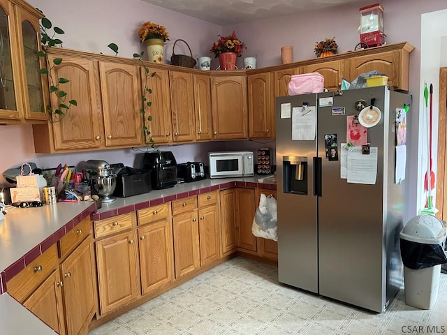 kitchen with glass insert cabinets, light floors, stainless steel refrigerator with ice dispenser, white microwave, and brown cabinetry