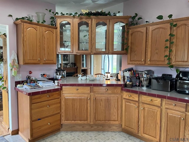 kitchen with glass insert cabinets, tile counters, a peninsula, and brown cabinets