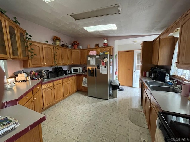 kitchen with a sink, glass insert cabinets, brown cabinetry, white microwave, and stainless steel refrigerator with ice dispenser