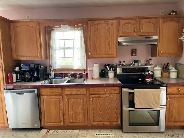 kitchen with stainless steel appliances, under cabinet range hood, a sink, visible vents, and tile countertops