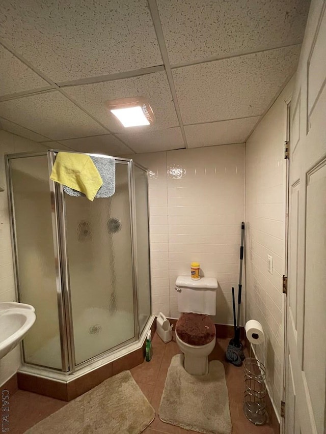 full bathroom featuring tile patterned floors, a drop ceiling, toilet, and a stall shower