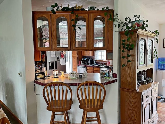 kitchen with appliances with stainless steel finishes, a kitchen bar, a peninsula, and glass insert cabinets
