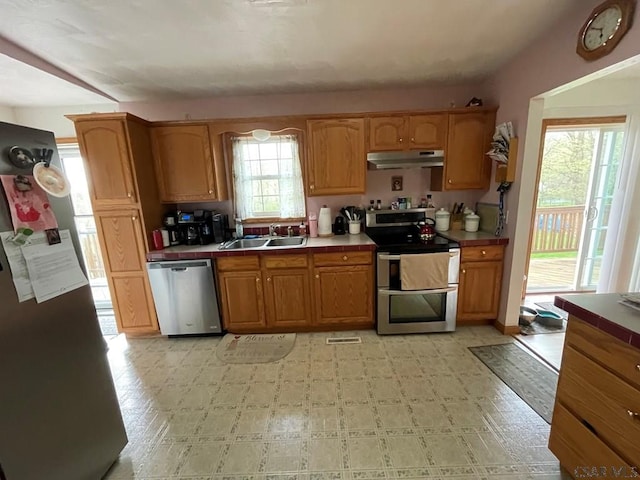 kitchen with a sink, appliances with stainless steel finishes, tile counters, under cabinet range hood, and light floors