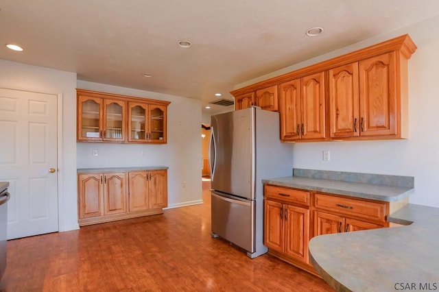 kitchen featuring visible vents, wood finished floors, brown cabinets, and freestanding refrigerator