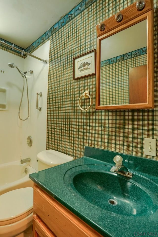 bathroom featuring toilet,  shower combination, vanity, and wallpapered walls