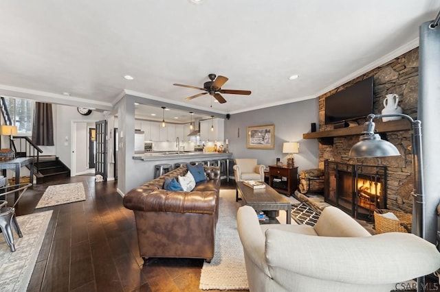 living room with a fireplace, ornamental molding, ceiling fan, wood finished floors, and baseboards