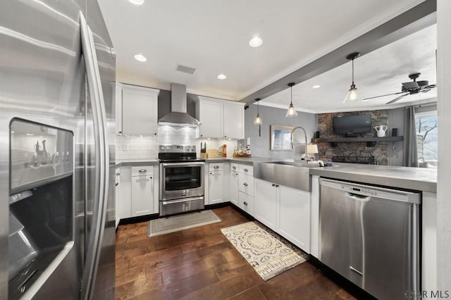 kitchen with decorative backsplash, dark wood-style floors, stainless steel appliances, wall chimney range hood, and a sink