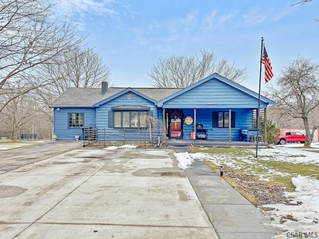 view of front of property with covered porch, roof with shingles, driveway, and a chimney