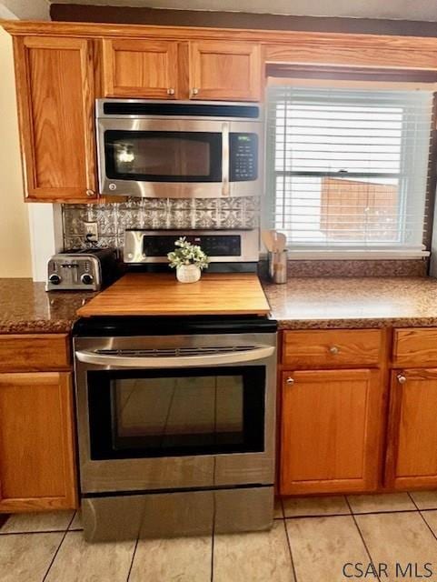 kitchen featuring light tile patterned flooring, appliances with stainless steel finishes, and dark stone countertops