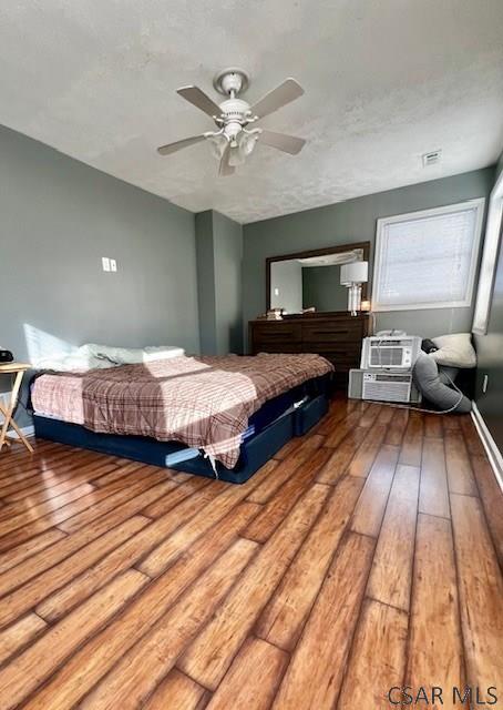 bedroom featuring hardwood / wood-style floors, a textured ceiling, a wall mounted air conditioner, and ceiling fan