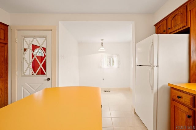 kitchen featuring freestanding refrigerator, light countertops, light tile patterned floors, brown cabinets, and pendant lighting