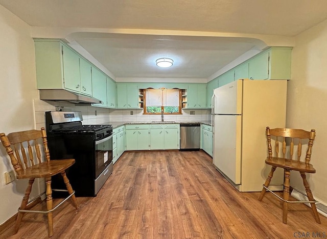 kitchen with appliances with stainless steel finishes, sink, backsplash, green cabinetry, and light hardwood / wood-style flooring