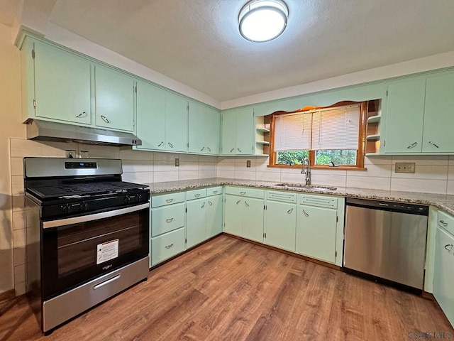 kitchen with sink, tasteful backsplash, green cabinets, stainless steel appliances, and light hardwood / wood-style floors