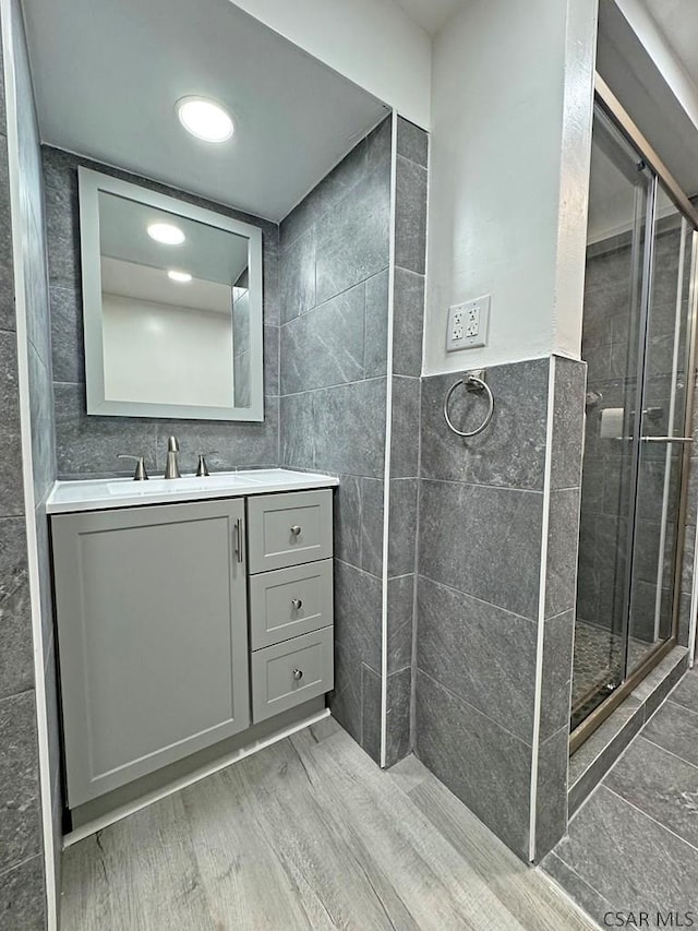 bathroom featuring vanity, wood-type flooring, tile walls, and an enclosed shower