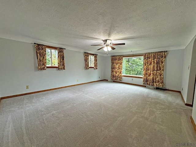 empty room with a healthy amount of sunlight, light colored carpet, a textured ceiling, and ceiling fan