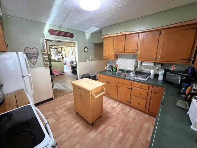 kitchen with a textured ceiling, a sink, white appliances, and light wood-style floors