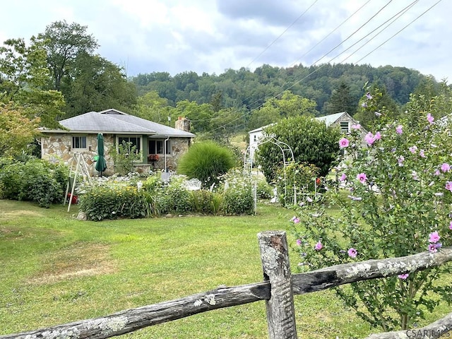 view of front facade featuring a front lawn, a view of trees, and stone siding