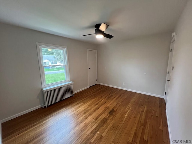 empty room featuring radiator, baseboards, wood finished floors, and a ceiling fan