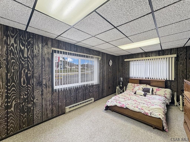 bedroom with a drop ceiling, wooden walls, carpet, and baseboard heating