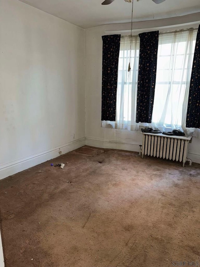 carpeted empty room featuring ceiling fan and radiator