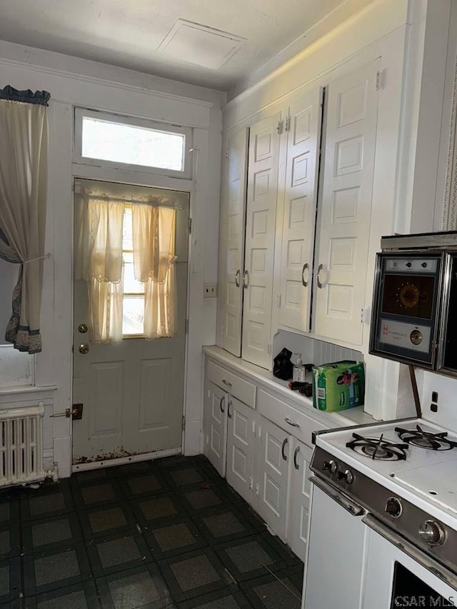 kitchen with radiator heating unit, white range with gas stovetop, and white cabinets