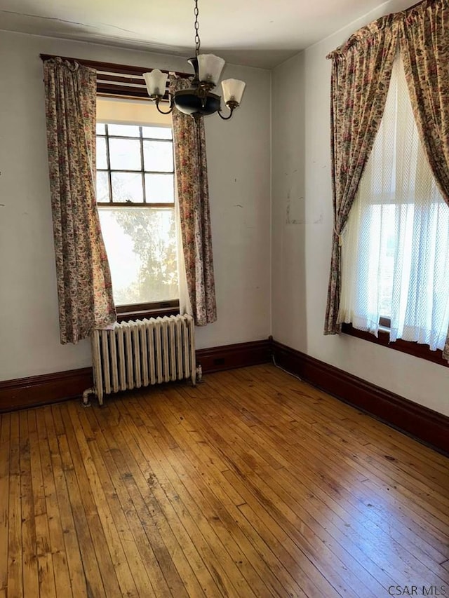 unfurnished dining area featuring wood-type flooring, a healthy amount of sunlight, radiator heating unit, and a chandelier